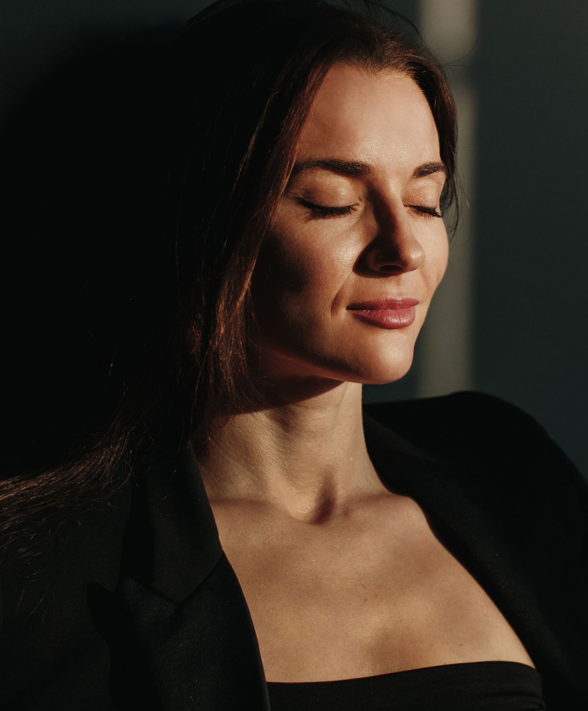 Woman with closed eyes, peaceful expression in light.