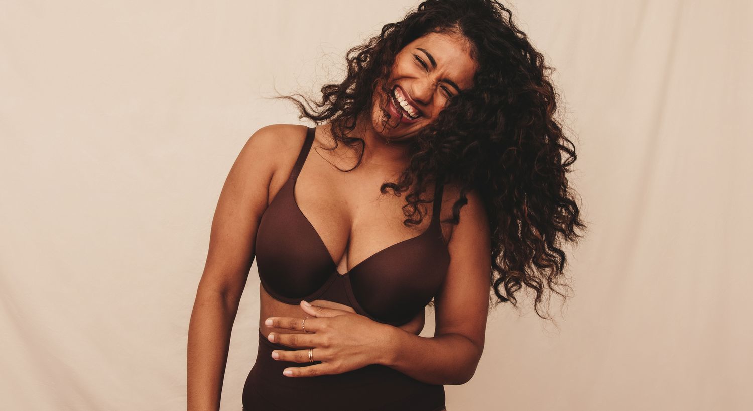 Woman smiling in a brown bra against beige background.